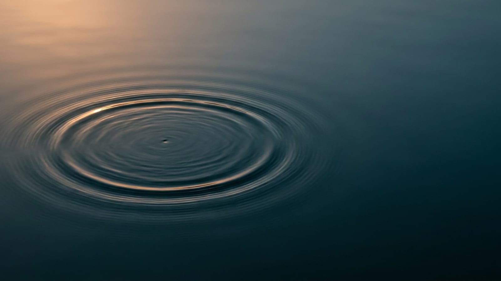 Abstract editorial cover image: concentric ripples spreading across a still water surface under soft directional light, used to represent focused energy delivered in layers. Illustrative only; not a clinical image.